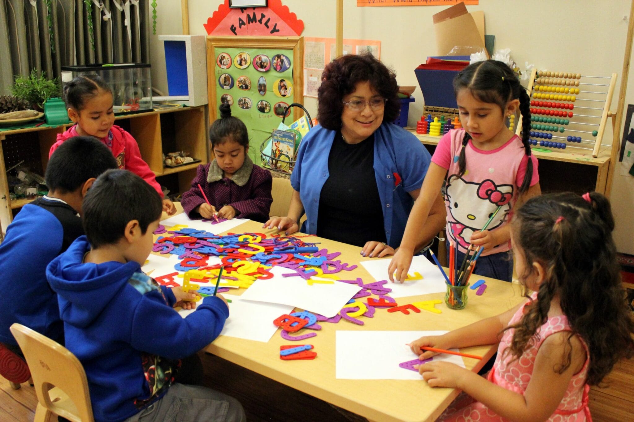 An early educator is sitting at a table with children, guiding them through an activity.