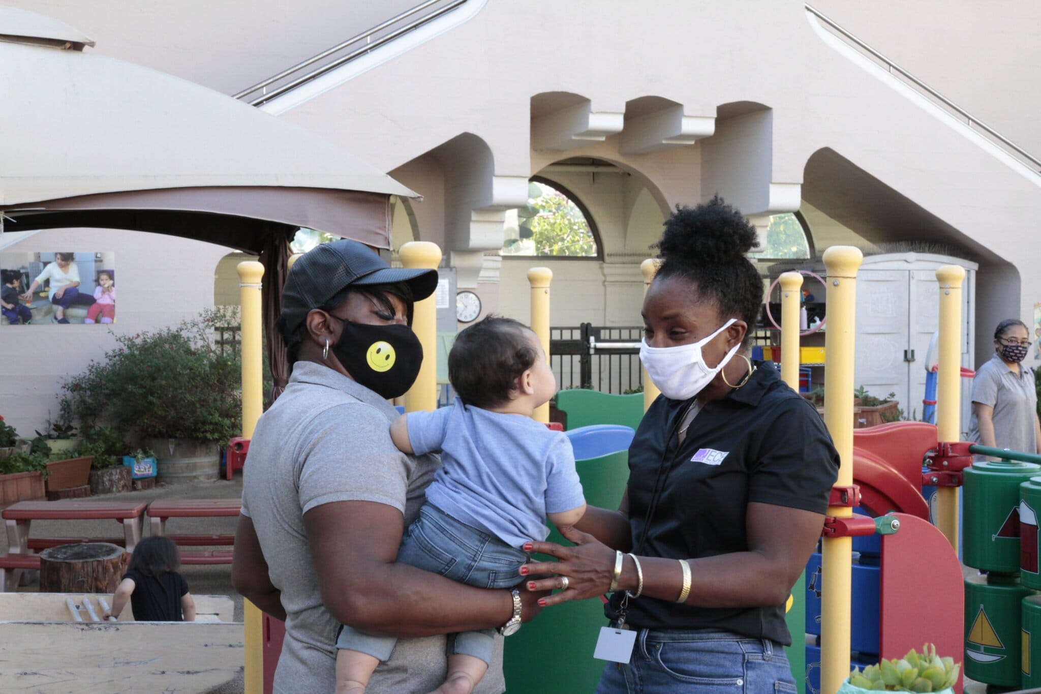 Two early educators with masks are interacting with a child.