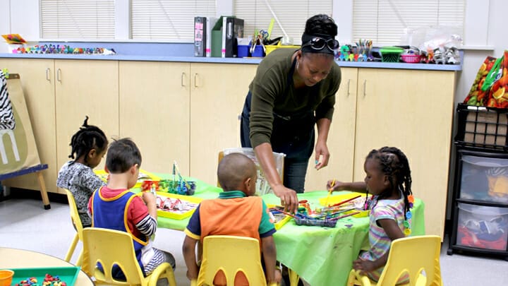 An early educator is helping a group of children at a table with paints.