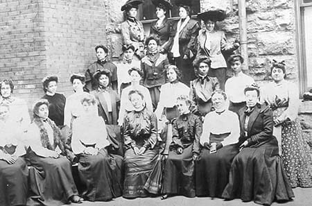 Formal portrait of women sitting outside a building.