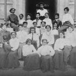 A group of Black women are seated outside of a building and posing for a formal black and white portrait.