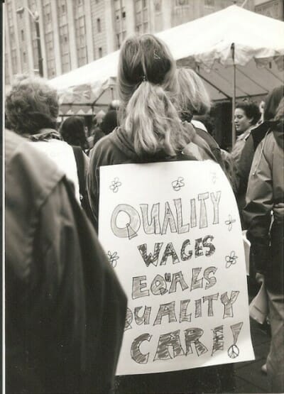 Woman at a rally with a sign on her back, "Quality Wages Equals Quality Care!"
