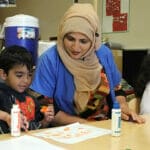 A child educator looks over the finished work of a student as she sits next to them.