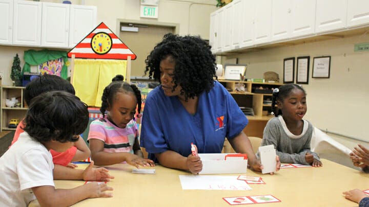 An early educator is looking over a child as they play a flashcard game.