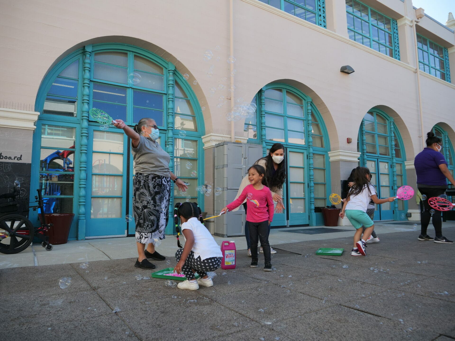 Adult early educators and children playing with bubbles outside