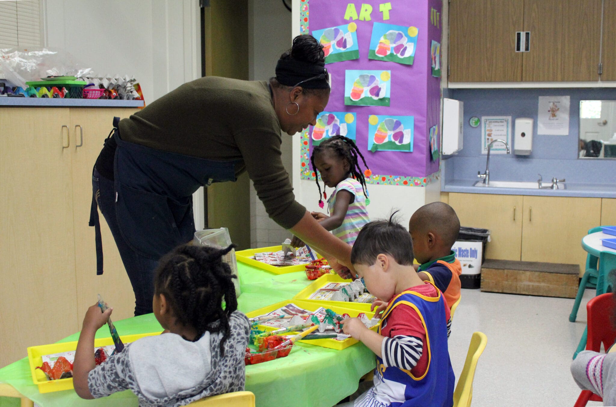 African American early educator helps children working at a table in a preschool classroom