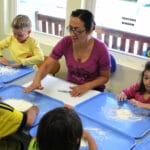 An early educator playing with flour at a table with children