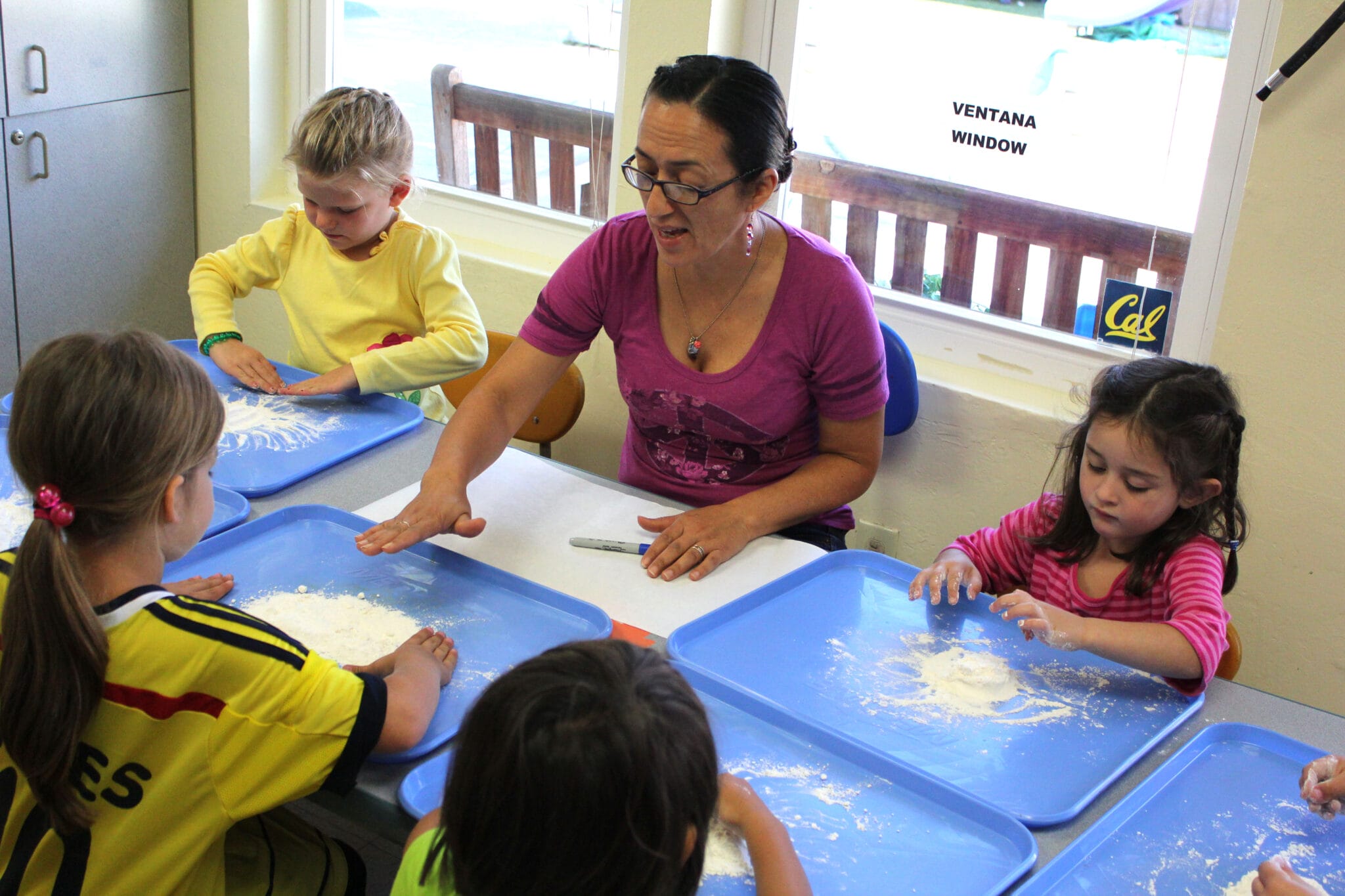 An early educator playing with flour at a table with children