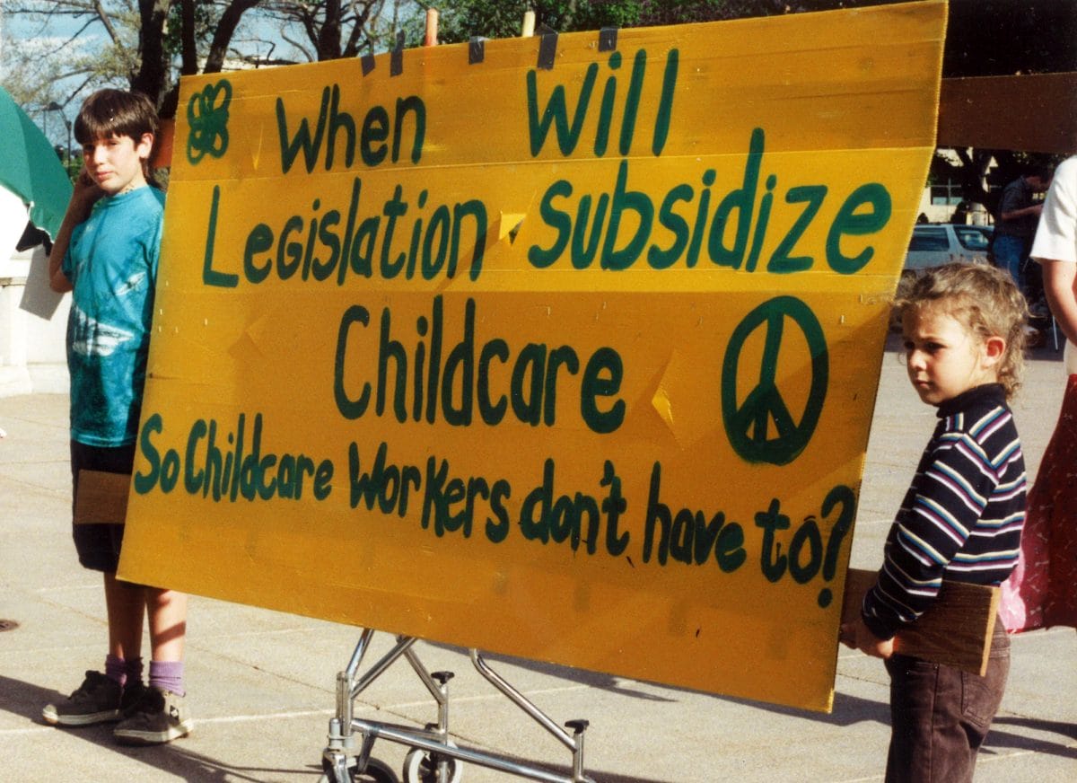 1992 Children Carrying Large Yellow Banner That Reads “When Will Legislation Subsidize Childcare So Childcare Workers Don’t Have To ”