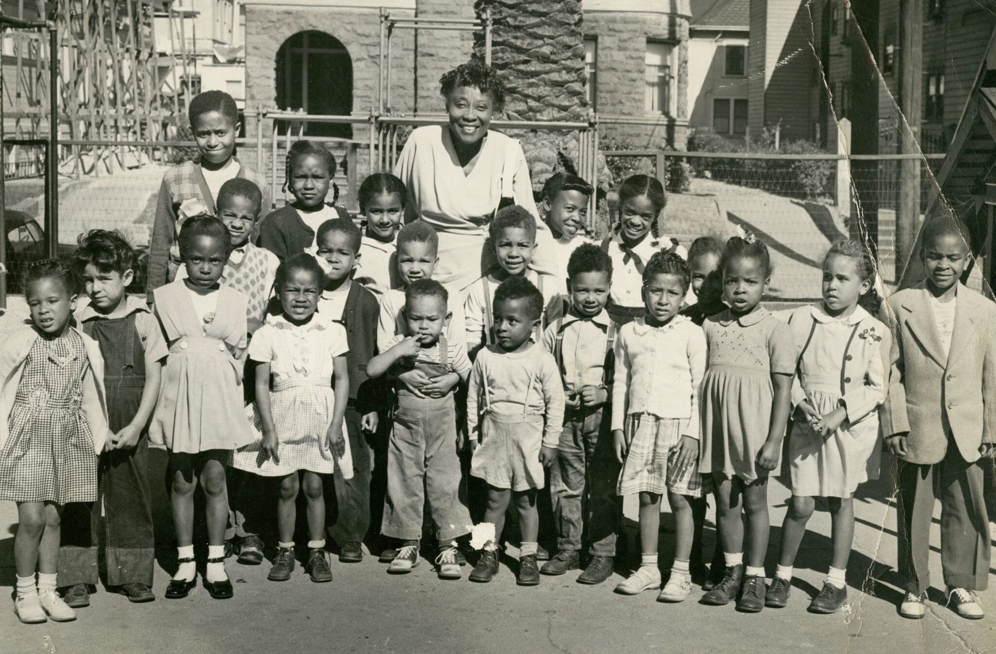 Early black teacher posing outside with black children for a picture.