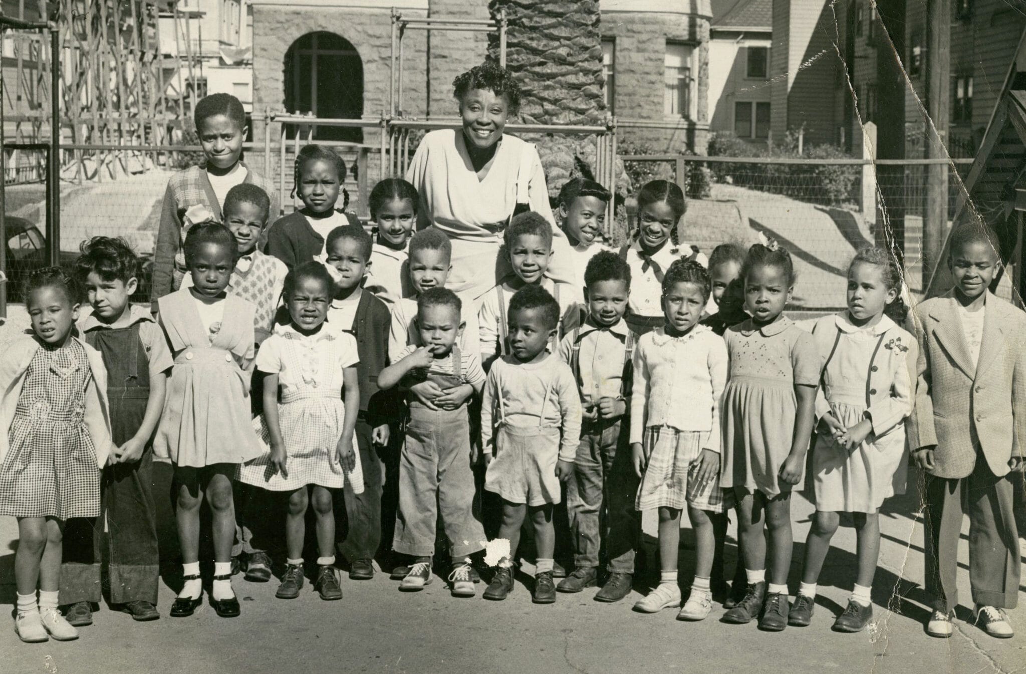 Early black teacher posing outside with black children for a class picture.