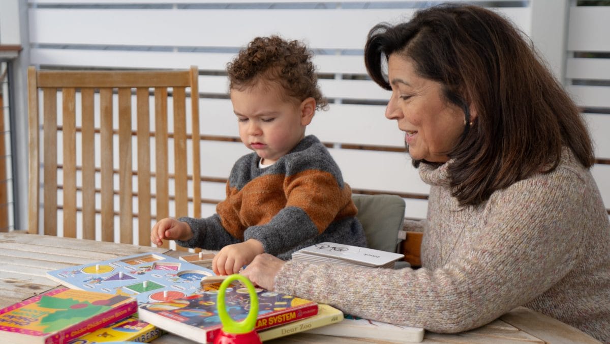 An infant with a child care provider sitting on a table reading a book together.