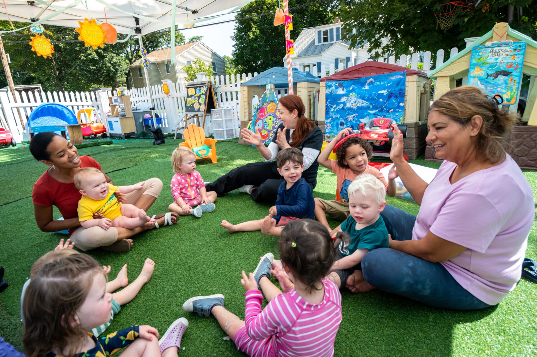 A group of educators sits waving hands in a circle with children.