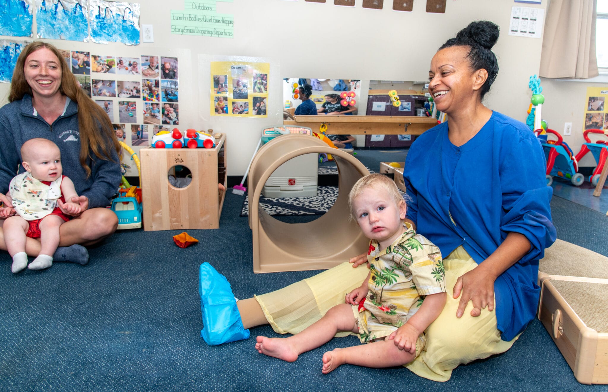 Two child-care workers play with a baby in each of their laps.