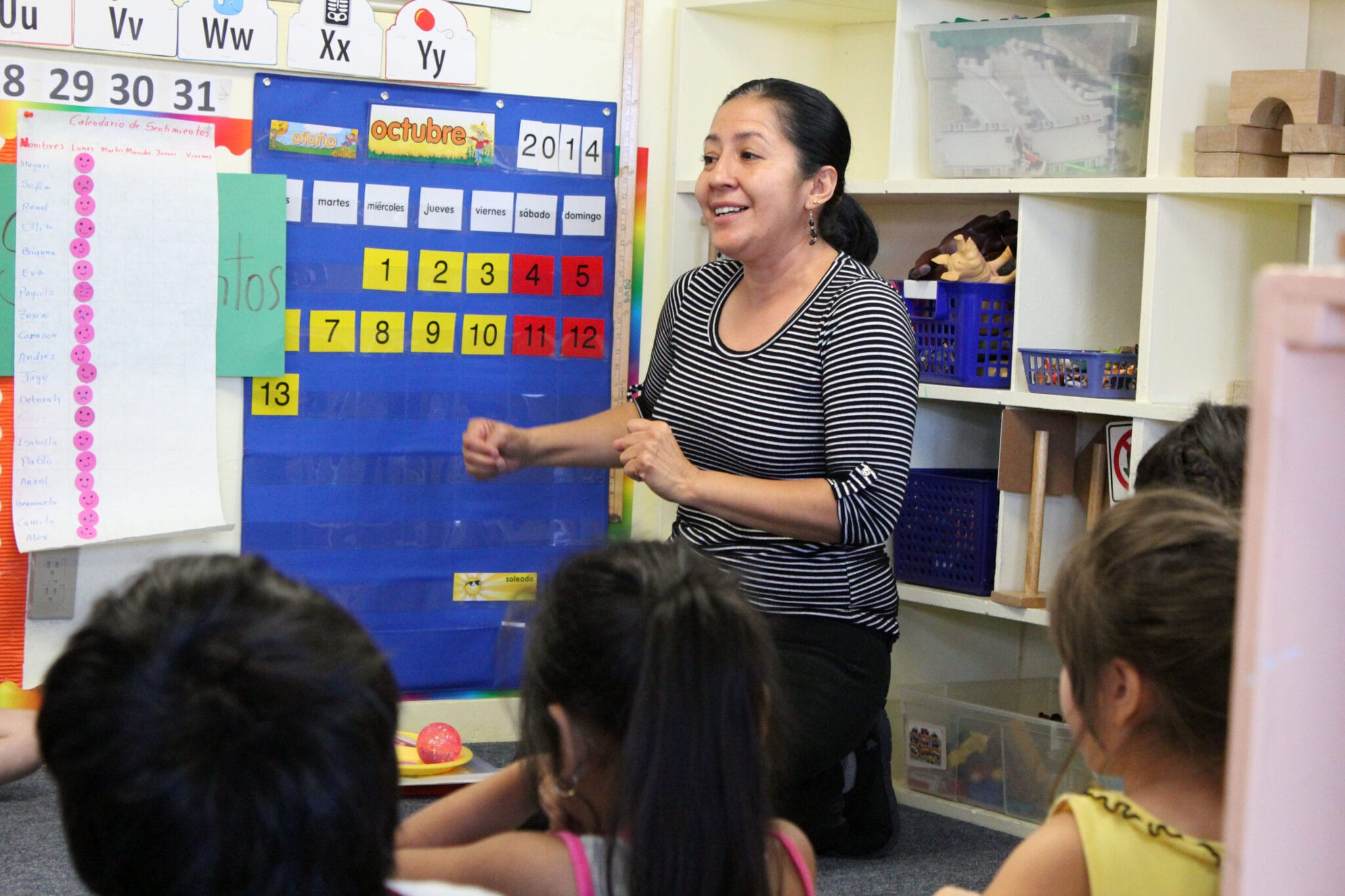 A teacher standing in-front of an interactive board, while teaching to younger children.