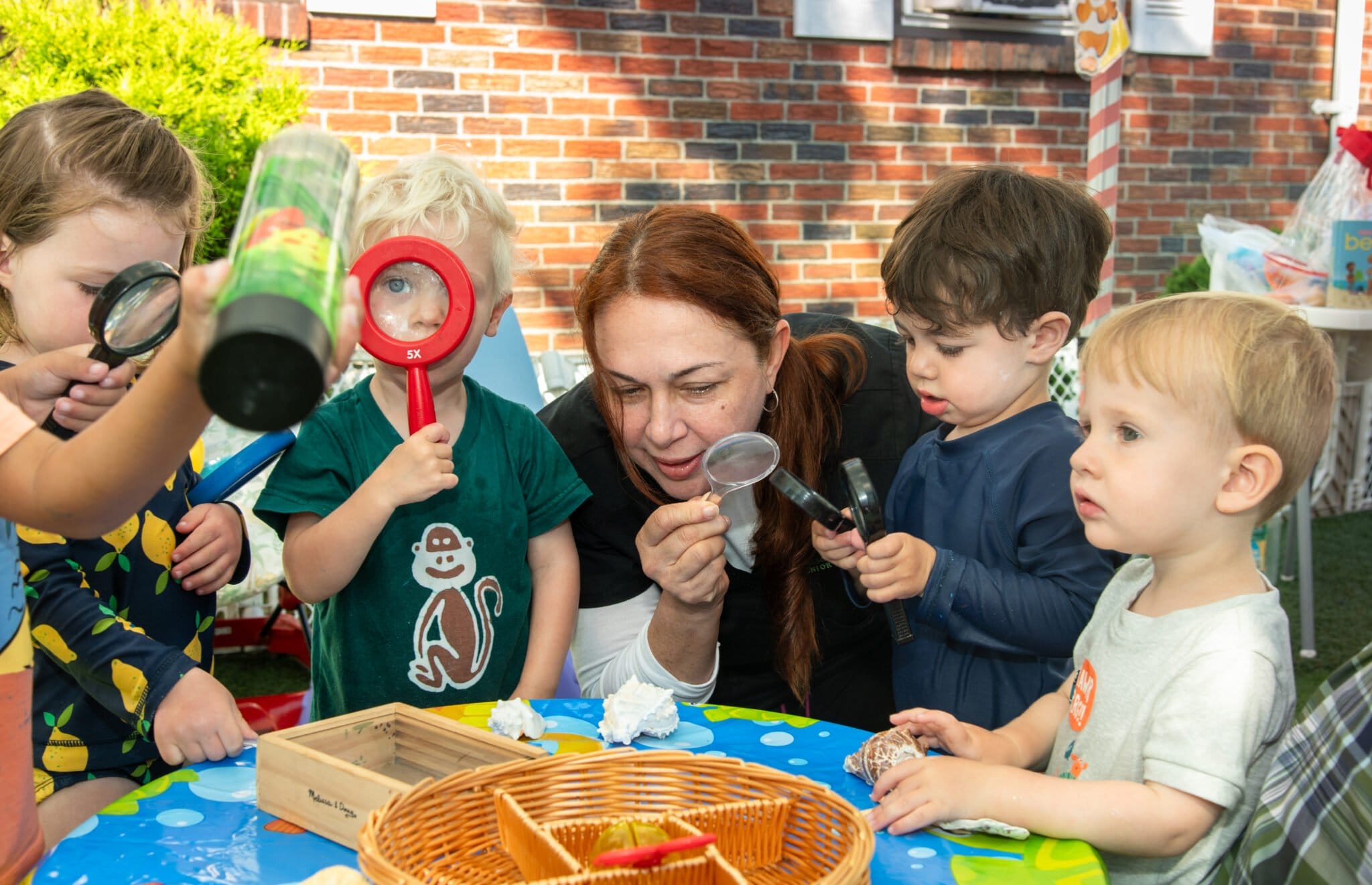 A child-care worker plays with a group of children as they play with magnifying glasses.