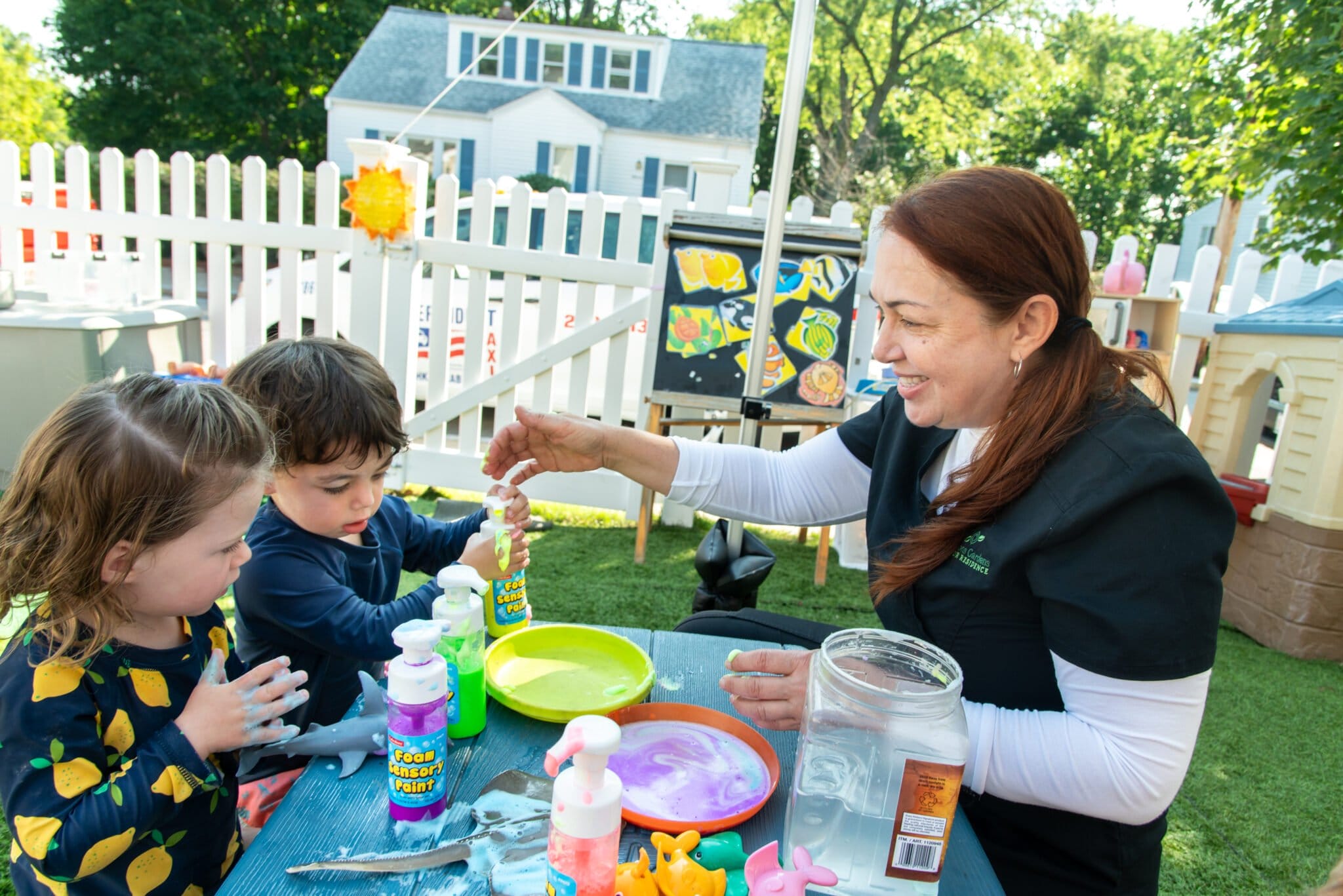 An early educator helps a group of children paint with foam paints.