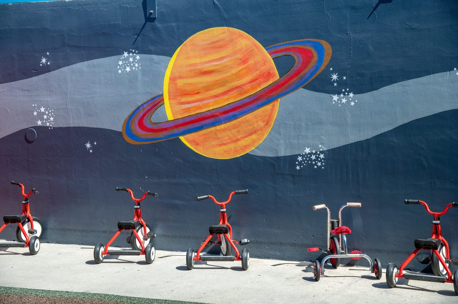 Six red tricycles parked against the wall of a preschool.
