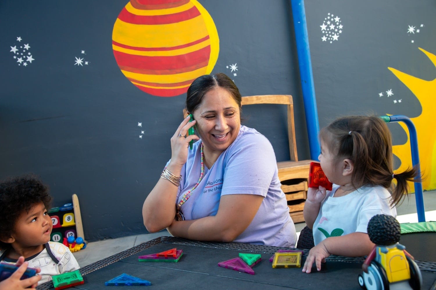 A teacher and young child hold up a plastic toy up to their ears.